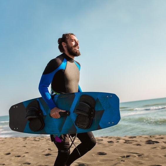 Bearded man runs on the beach while carrying a surfboard