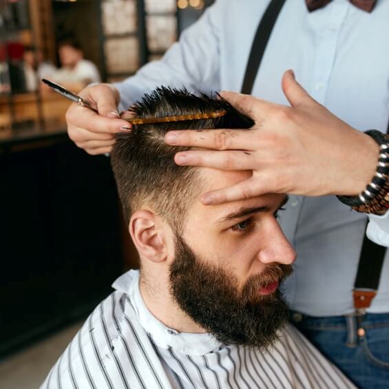 Barber cuts young man’s hair in a barbershop.