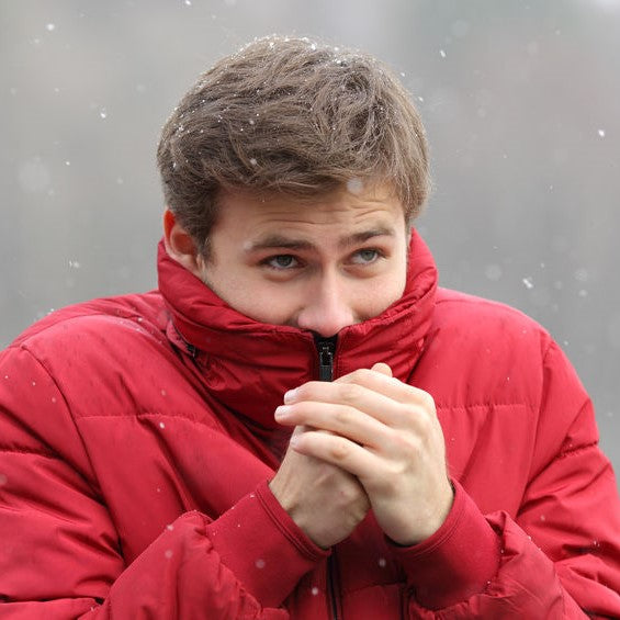 Man shivering in cold winter snowfall and rubbing hands
